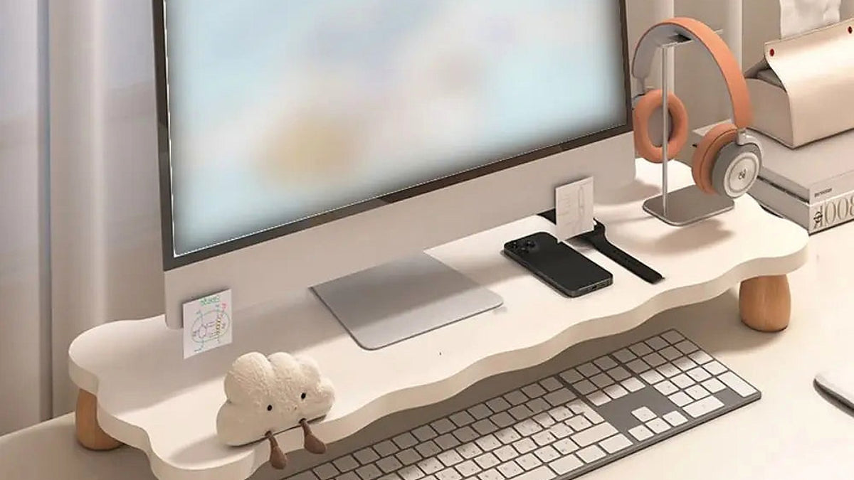 A monitor raised on a wooden riser above a keyboard on a light desk