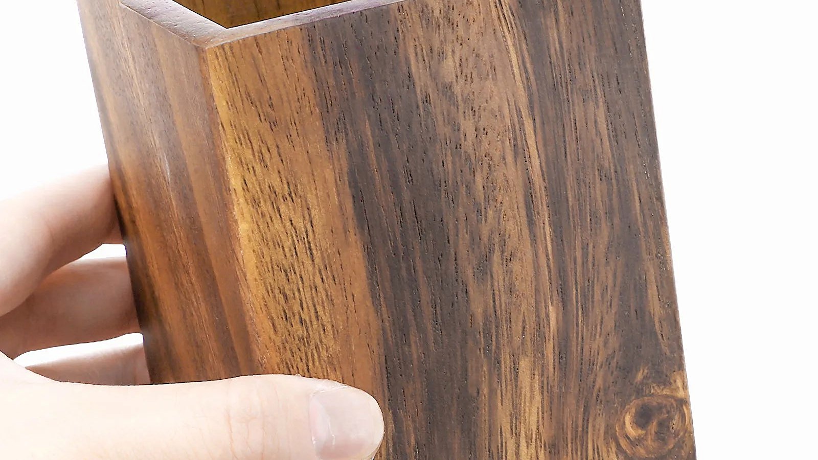A hand holding a solid walnut pen cup, showing the grain and end grain