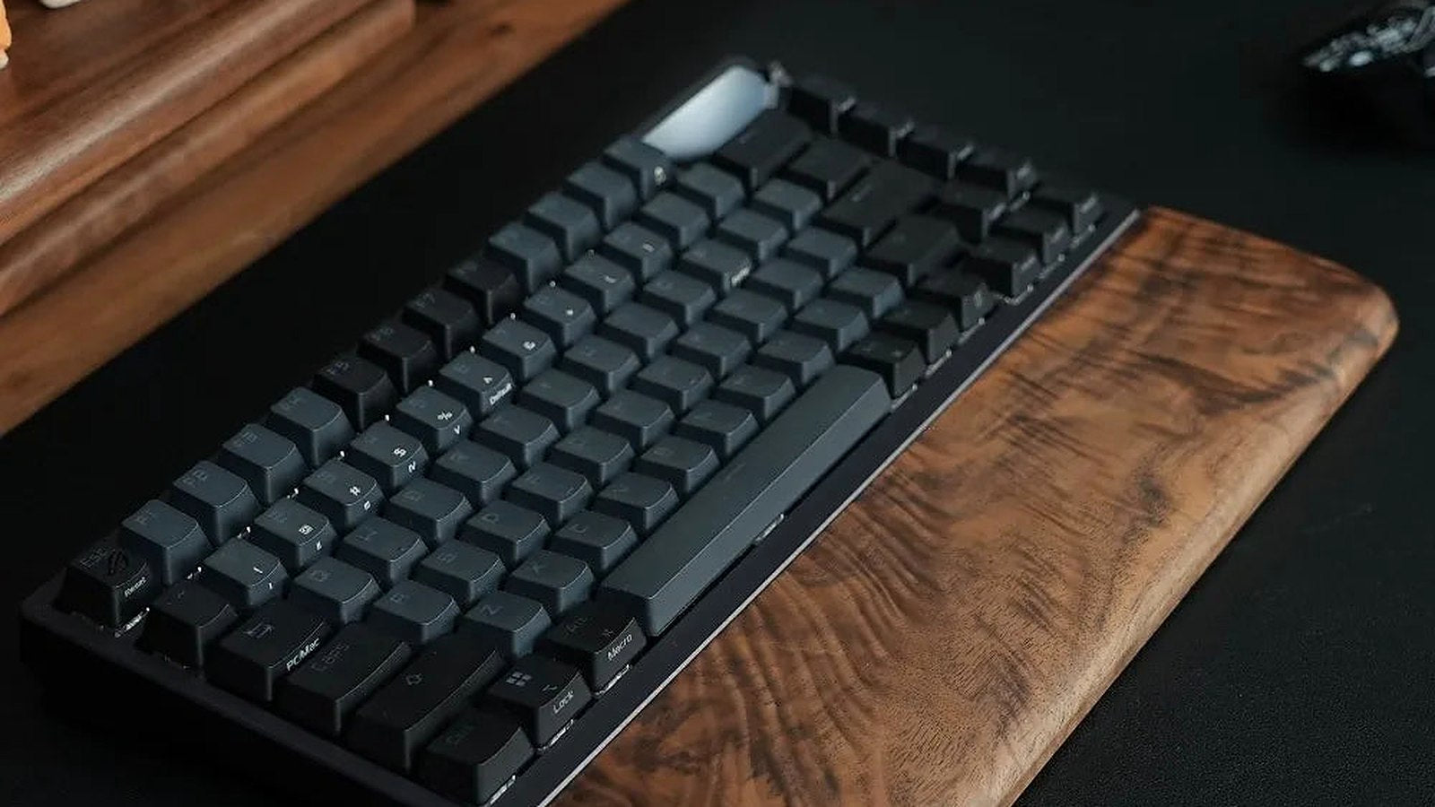 A solid walnut wrist rest in front of a mechanical keyboard on a dark desk